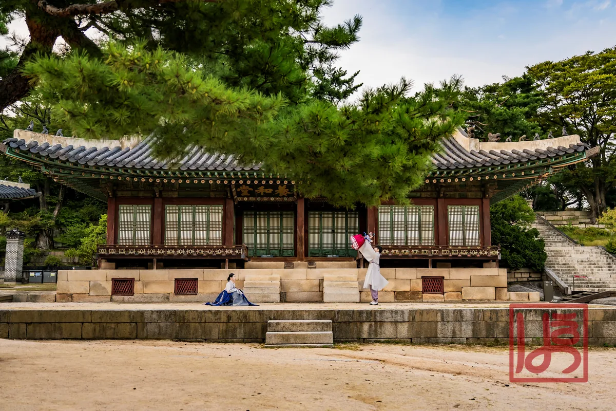 고궁 마당에서 남색 치마와 회색 저고리를 입고 아이를 안아 올리는 모습