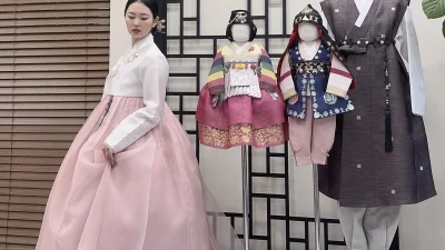 연분홍 치마와 흰 저고리의 우아한 성인 한복, 뒤로 돌잔치 색동 한복들이 진열돼 있다