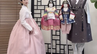 연분홍 치마와 흰 저고리의 우아한 성인 한복, 뒤로 돌잔치 색동 한복들이 진열돼 있다
