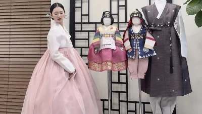 연분홍 치마와 흰 저고리의 우아한 성인 한복, 뒤로 돌잔치 색동 한복들이 진열돼 있다