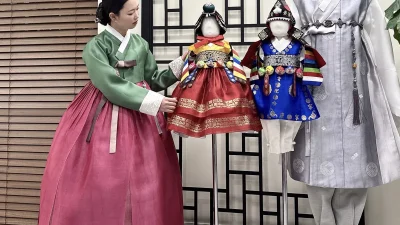 초록 저고리와 수복문 자주 치마의 여성 한복이 매장에 전시된 돌한복들과 어우러진 모습