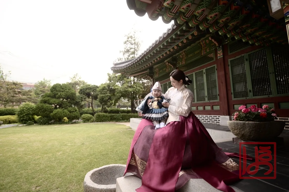 전복과 호건을 갖춘 돌한복과 진자주 치마 한복이 어우러진 한옥 배경